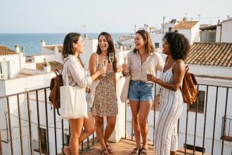 Groupe d'amies queer en vacances à Sitges portant un toast sur une terrasse ensoleillée avec vue sur la mer Méditerranée