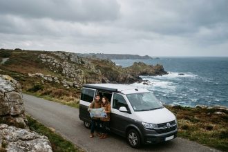 Couple en camping-car sur une route côtière bretonne face à l'océan Atlantique et des falaises de granit