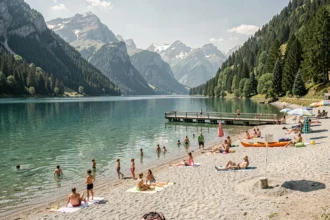 Vue panoramique d'une plage de lac alpin en Auvergne-Rhône-Alpes avec familles, baigneurs et montagnes enneigées en arrière-plan